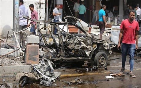 Iraqis walk past a destroyed vehicle at the scene of a car bomb blast in Baghdad, May 9, 2014. AFP Photo.