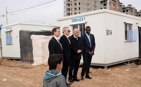 Officials pose in front of the new cabins at the Harshm Camp, as a refugee boy looks on. Photo by author.