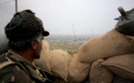 A kurdish Peshmerga fighter looks toward the city of Shingal from behind sand bags. AP file photo.