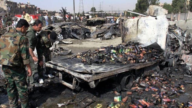 Syrian soldiers check a burned truck in front of a damaged military intelligence building where two bombs exploded, in Damascus, Syria in 2012. AP photo. 