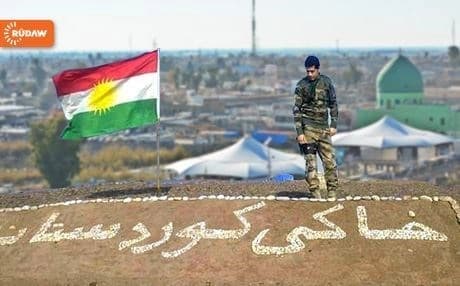 With Kirkuk in background, a Kurdish soldier stands before a sign that reads, “Land of Kurdistan.” Photo: Rudaw
