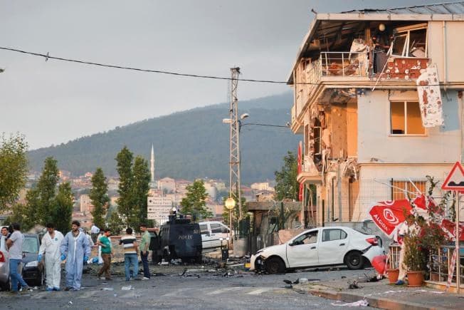 Turkish police officers work at the site of an explosion at a police station, seen right, in Istanbul's Sultanbeyli neighborhood, early Monday, Aug. 10, 2015. Photo by AP. 