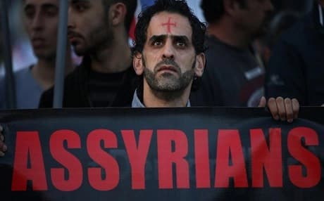 An Assyrian man with a red cross painted on his forehead holds a banner as he walks during a protest of several hundred people in solidarity with Christians abducted in Syria and Iraq. (File photo: AP)