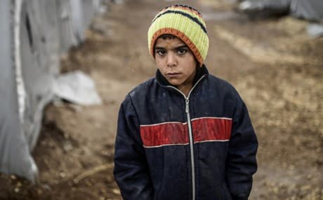 A Kurdish refugee boy stands outside his tent during a rainy day. AP file photo