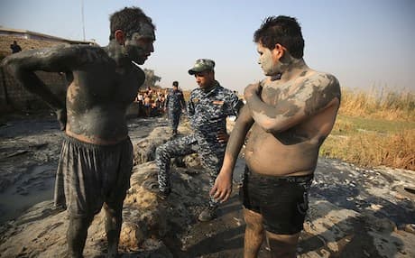 A member of the Iraqi federal police watches two men rubbing themselves in the healing mud of Hamam Alil south of Mosul. Photo: Rudaw