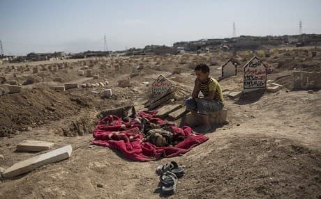 In this image at a Mosul graveyard on Oct. 2, 2017, 8-year-old Mohammed Mahmoud sits next to the remains of his uncle, Omar, whose family says he was shot by Islamic State fighters while trying to flee the final battle against the group. Photo: AP Photo/Bram Janssen