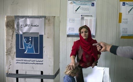 A volunteer points out the place where a displaced woman from Sinjar can cast her vote in the parliamentary elections at a polling site in an IDP camp outside Erbil, Saturday, May 12, 2018. Photo: Bram Janssen / AP
