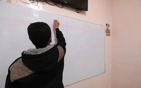 A teenage boy writes on a white board at the Hori rehabilitation centre for former ISIS child fighters in Tal Maarouf, Hasaka. Photo: Delil Souleiman/AFP