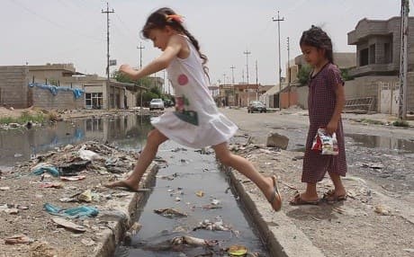 Girls jump across trash-strewn gutter in Kirkuk. Photo: Rudaw