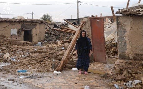 A woman stands outside the ruins of her home in Kermanshah. Photo: Tahir Gholami