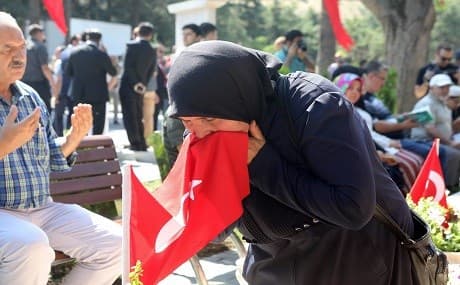 A woman kisses a Turkish flag and a man prays, as people visit graves of their relatives who died during the failed coup on July 15, 2016 in Turkey, during a ceremony marking the second anniversary of failed coup, on July 15, 2018 in Ankara. Photo: Adem Altan / AFP 