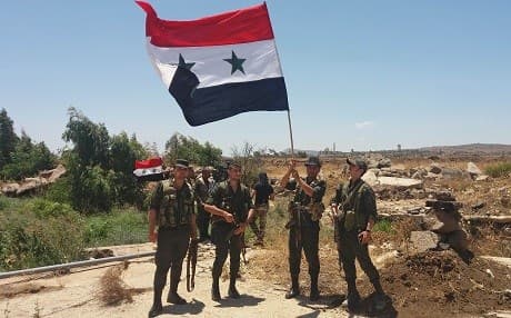 A handout picture released by the official Syrian Arab News Agency (SANA) on July 26, 2018 shows Syrian army soldiers carrying the national flag in the village of Hamidiya in the southern province of Quneitra. Photo: AFP/HO/SANA