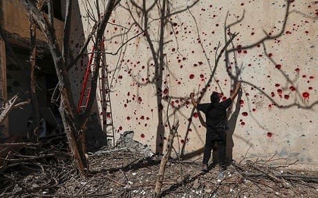 A man sprays red paint in the pockmarks left by shrapnel in the wall of the KDP-I headquarters in Koya. Photo: Safin Hamed/AFP