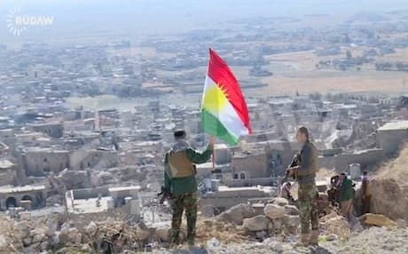 A Kurdish Peshmerga soldier holding a Kurdistan flag on Mount Shingal. Photo: Rudaw/File