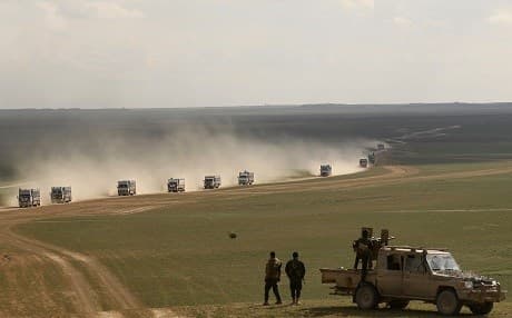Syrian Democratic Forces stand guard as a convoy of truck transports civilians fleeing the battered ISIS holdout of Baghouz on February 11, 2019. Photo: Delil Souleiman | AFP
