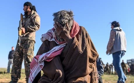 A member of the Kurdish-led SDF stands by as a man sits with his palm on his face, after leaving the Islamic State (ISIS) holdout of Baghouz, Syria on March 1, 2019. Photo: Bulent Kilic | AFP