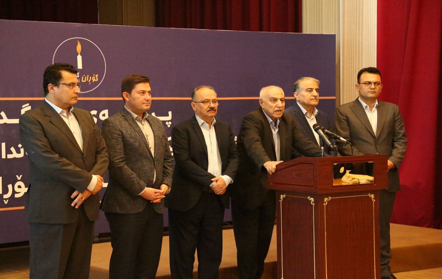 Newly elected members of Gorran’s Executive Body stand beside reelected leader of the party Omar Saeed Ali speaking at the podium following the party’s internal elections. Photo: Briar Namiq