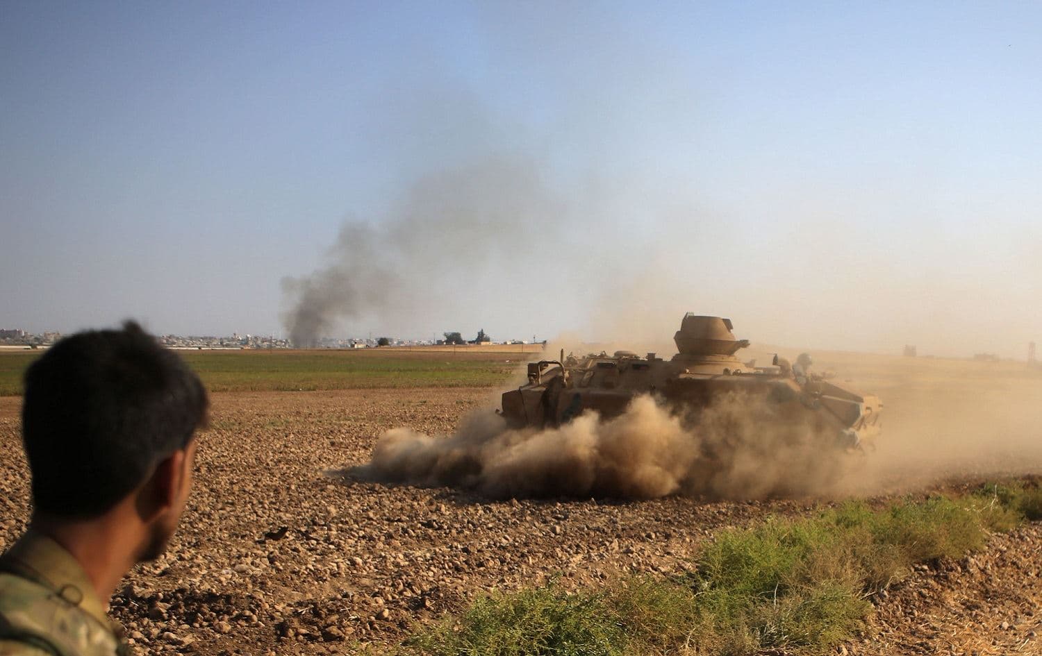 A Syrian fighter with the Turkey-backed forces watches an armoured personnel carrier manoeuvring on the outskirts of the border Syrian town of Tal Abyad, October 13, 2019. Photo: Bakr al-Kasem / AFP