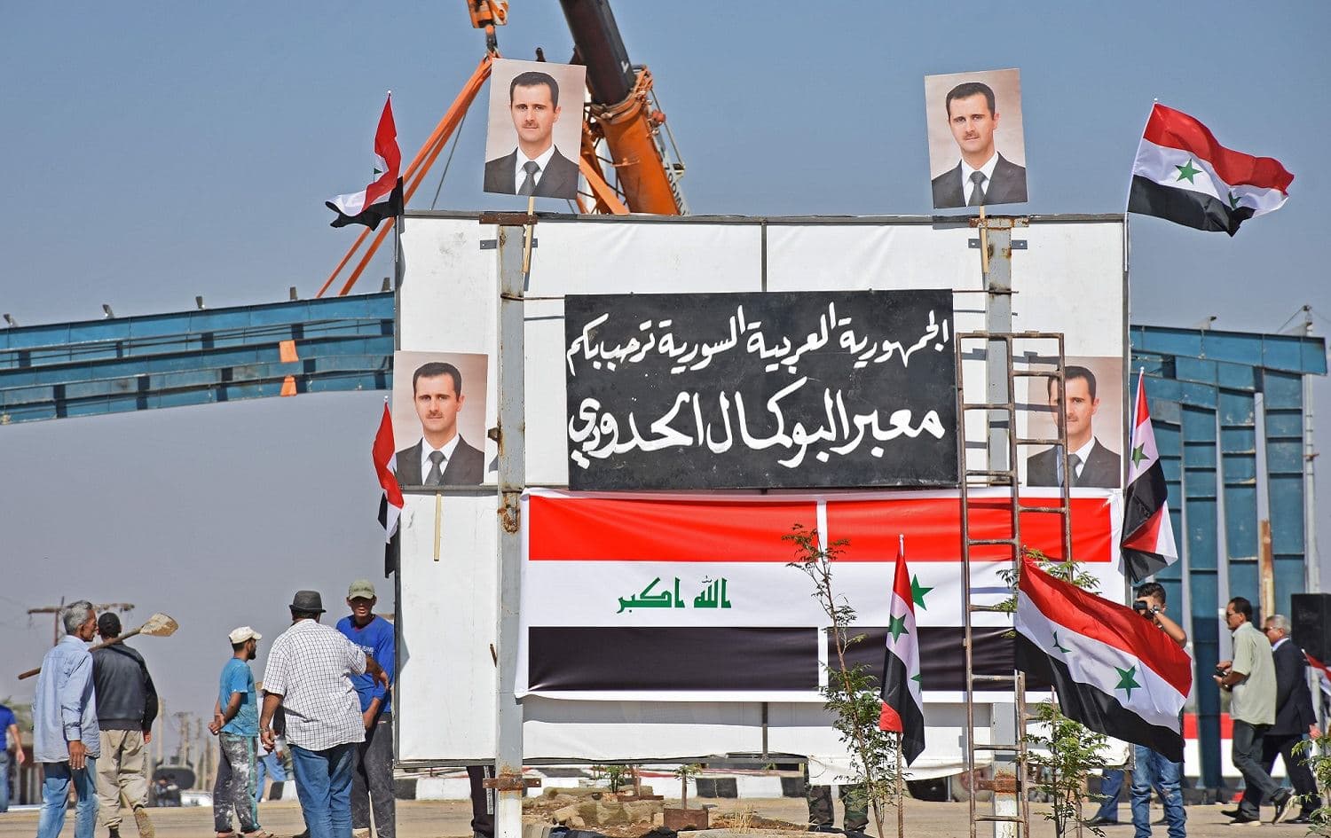 Posters of Syria’s President Bashar al-Assad and the Syrian (R) and Iraqi national flags are pictured at the border-crossing between Al-Qaim in Iraq and Albu Kamal in Syria from the Iraqi side, September 30, 2019. Photo: Moadh al-Dulaimi / AFP