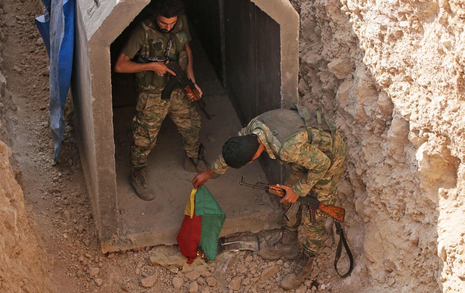 Turkish-backed Syrian fighters burn a flag of the northern Syria autonomous region at the entrance of a tunnel, said to have been built by Kurdish fighters, in the Syrian border town of Gire Spi (Tal Abyad), on October 21, 2019. Photo: Bakr Alkasem/AFP