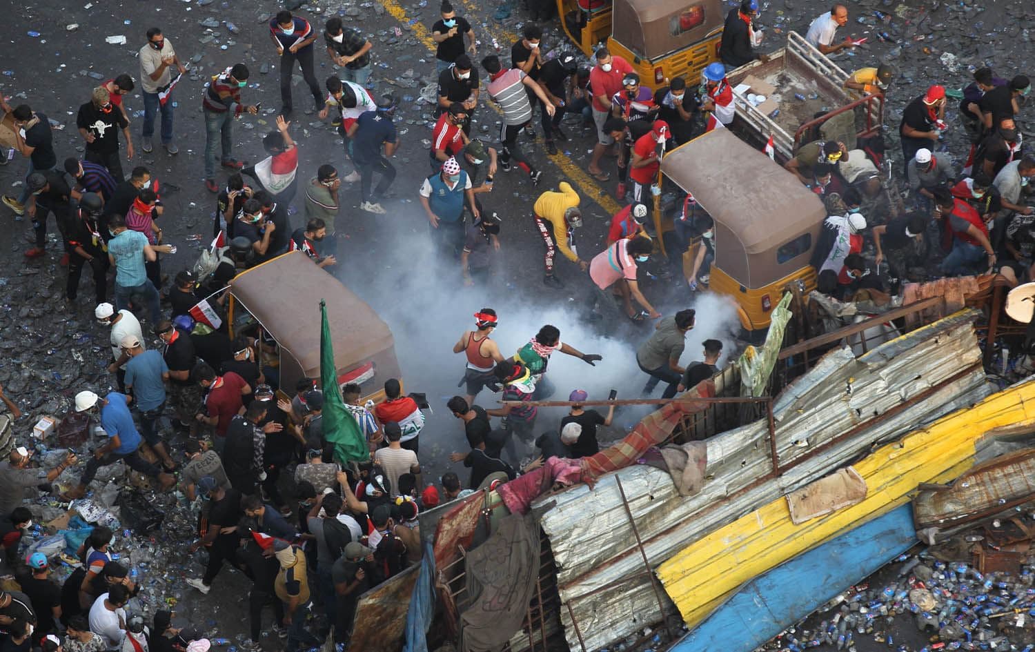 Iraqi anti-government protesters stand behind a barricade as security forces fire tear gas to keep demonstrators from storming the Green Zone, which hosts government offices and foreign offices, on October 28, 2019 in Baghdad. Photo: AFP