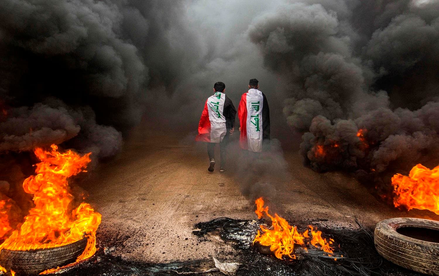 Anti-government protesters walk into clouds of smoke from burning tires during a demonstration in the southern city of Basra on November 17, 2019. Photo: Hussein Faleh/AFP 