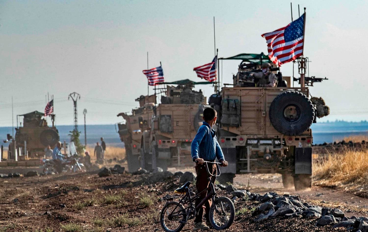 A Syrian boy on his bicycle looks at a convoy of US armoured vehicles patrolling fields near the northeastern town of Qahtaniyah at the border with Turkey, October 31, 2019. File photo: Delil Souleiman / AFP