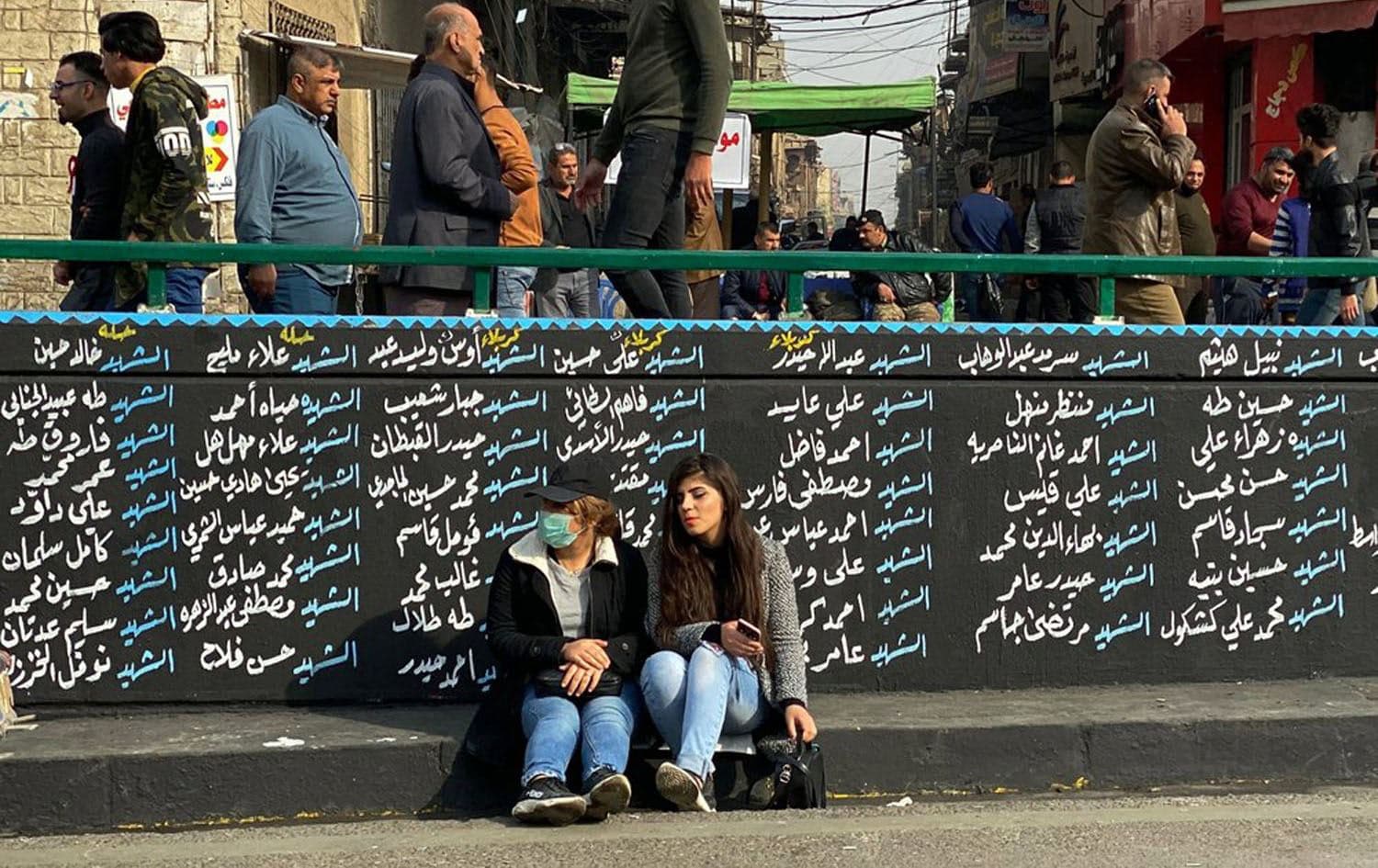 Women sit by a wall with names of anti-government protesters who have been killed in demonstrations in Tahrir Square during ongoing protests in Baghdad, Iraq. Photo via AP/Nasser Nasser