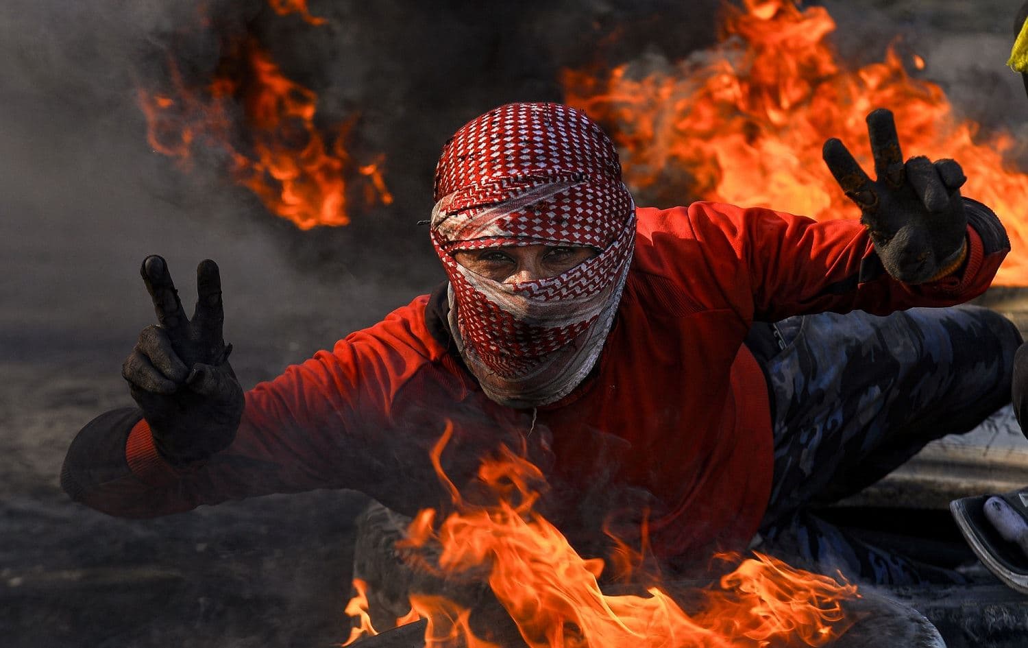 A protester flashes the victory gesture while posing by flaming tires in the central holy shrine city of Najaf, February 2, 2020. Photo: Haidar Hamdani / AFP