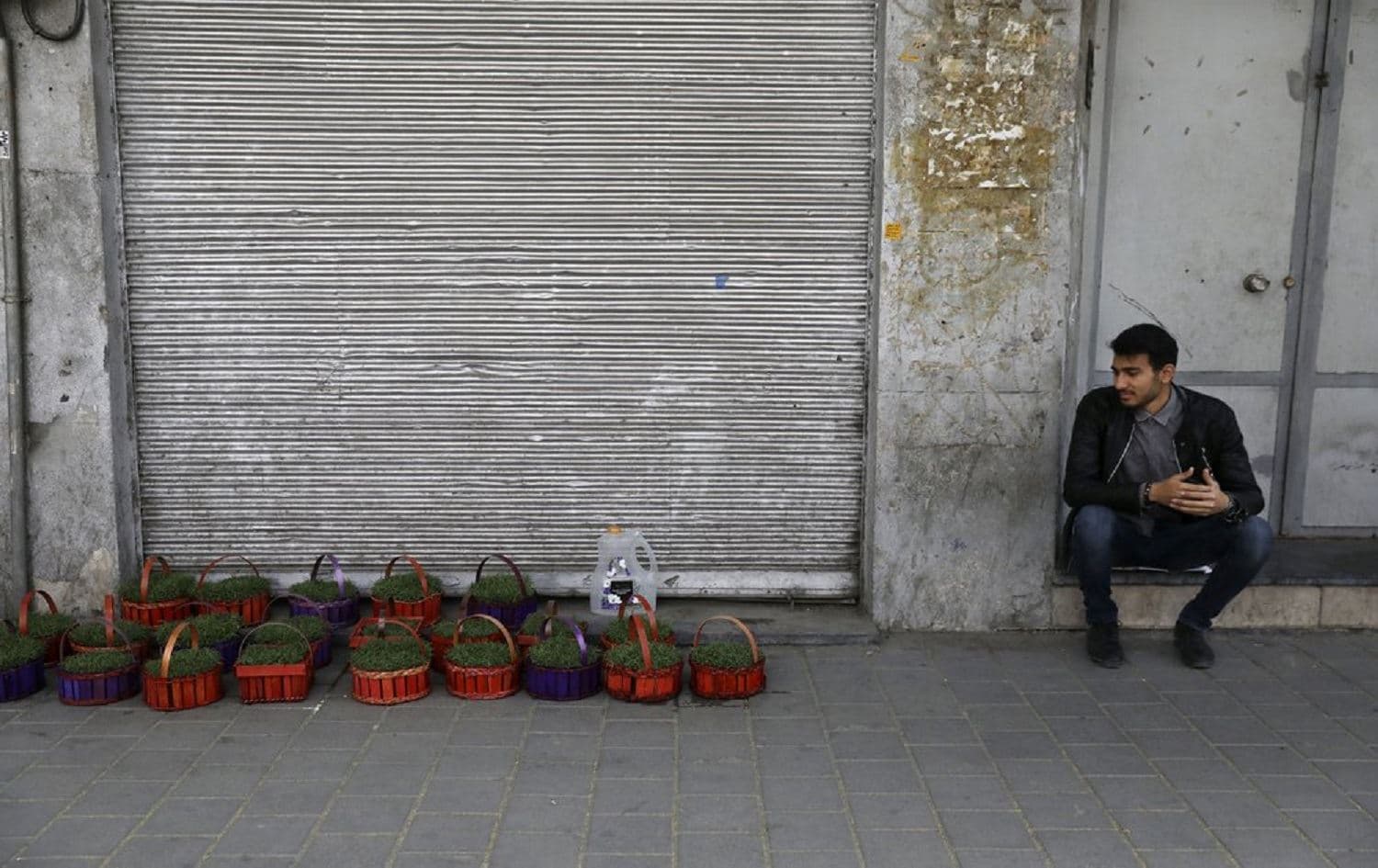  A vendor sits next to his baskets of grass shoots, an symbol of the Iranian New Year, in front of closed shops at Tehran's Grand Bazaar on March 17, 2020. Photo: Vahid Salemi/AP