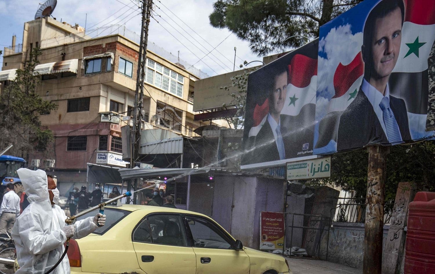 A member of the disinfection units of the semi-autonomous Syrian Kurdish administration sprays billboards of President Bashar al-Assad in Qamishli on March 24, 2020. Photo: Delil Souleiman / AFP
