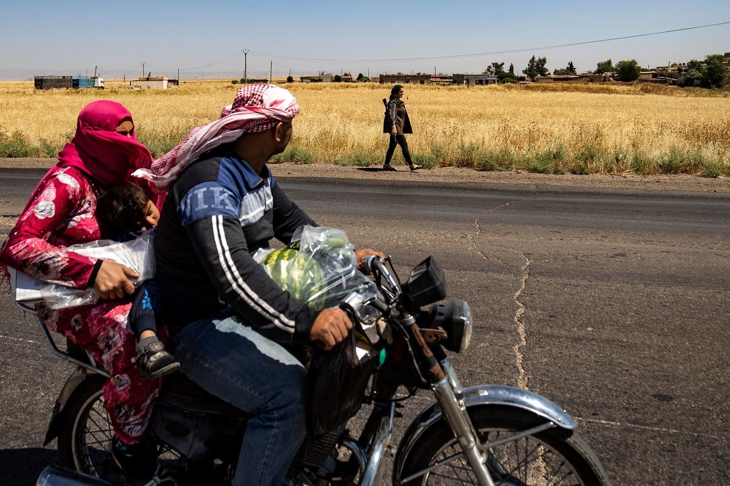 A family ride a motorcycle past a Kurdish female volunteer, from the newly formed Community Protection Forces, as she patrols a wheat field in the countryside east of Qamishli in Syria's northeastern Hasakah province. Photo: Delil Souleiman/ AFP