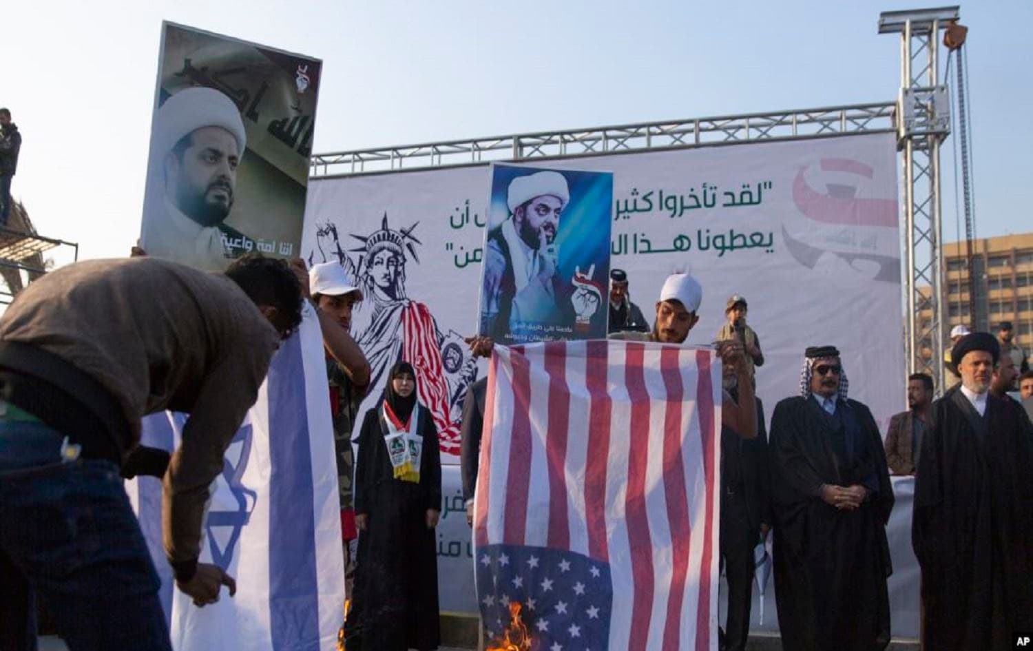 Iraqi protesters burn Israeli and US flags while others carry posters with pictures of Qais al-Khazali, during a rally for the Shiite group Asaib Ahl al-Haq, in Baghdad, Iraq, Saturday, Dec. 14, 2019.  Photo: Nasser Nasser / AP