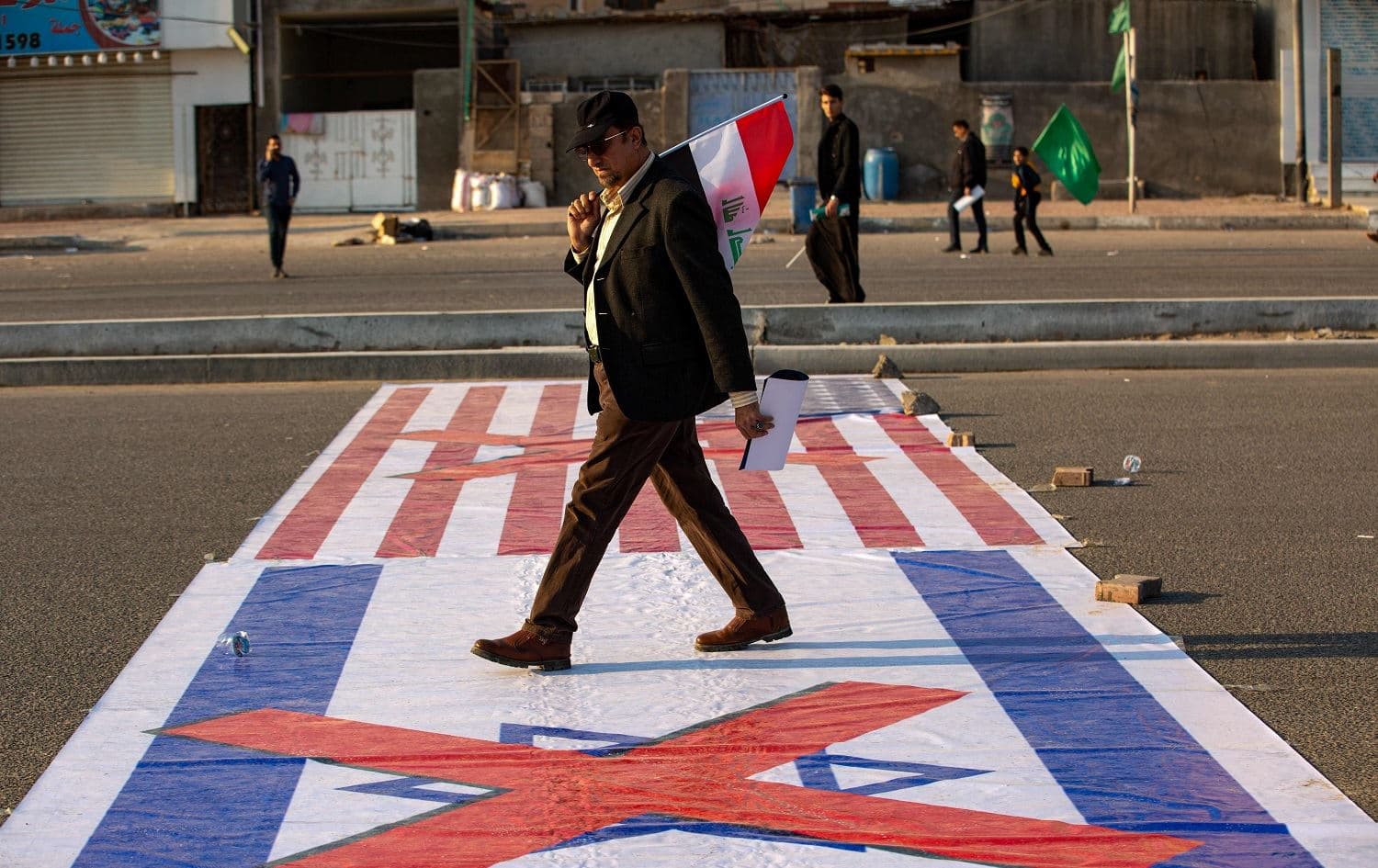 An Iraqi man steps over US and Israeli flags as he takes part in an event celebrating the inauguration of a street named after the late Iraqi commander Abu Mahdi al-Muhandis in Basra on January 8, 2021. Photo: Hussein Faleh/AFP