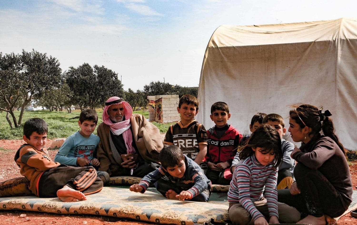 Abderrazaq Khatoun, rests with some of his 11 orphaned grandchildren, in an encampment in the village of Harbanoush, in the northern countryside of Syria's Idlib province, on March 11, 2021. Photo: Ahmad al-Atrash/AFP