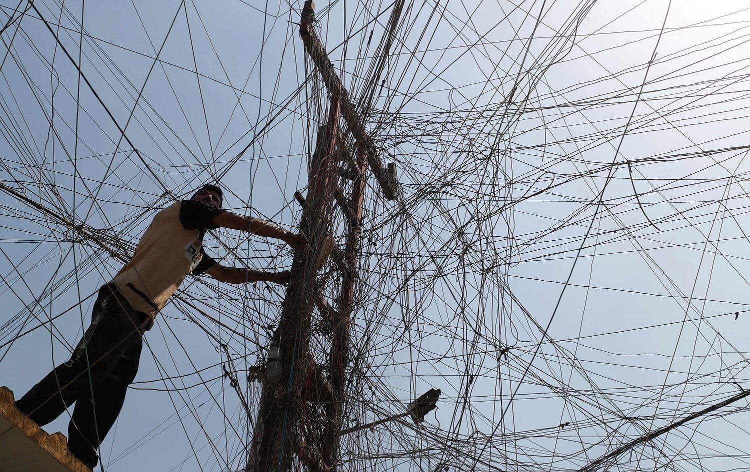 An Iraqi man connects overhead cables linking a generator to homes and businesses who can afford it in Sadr City, Baghdad, on July 2, 2021, amid power outages and soaring temperatures. Photo: Ahmad al-Rubaye/AFP