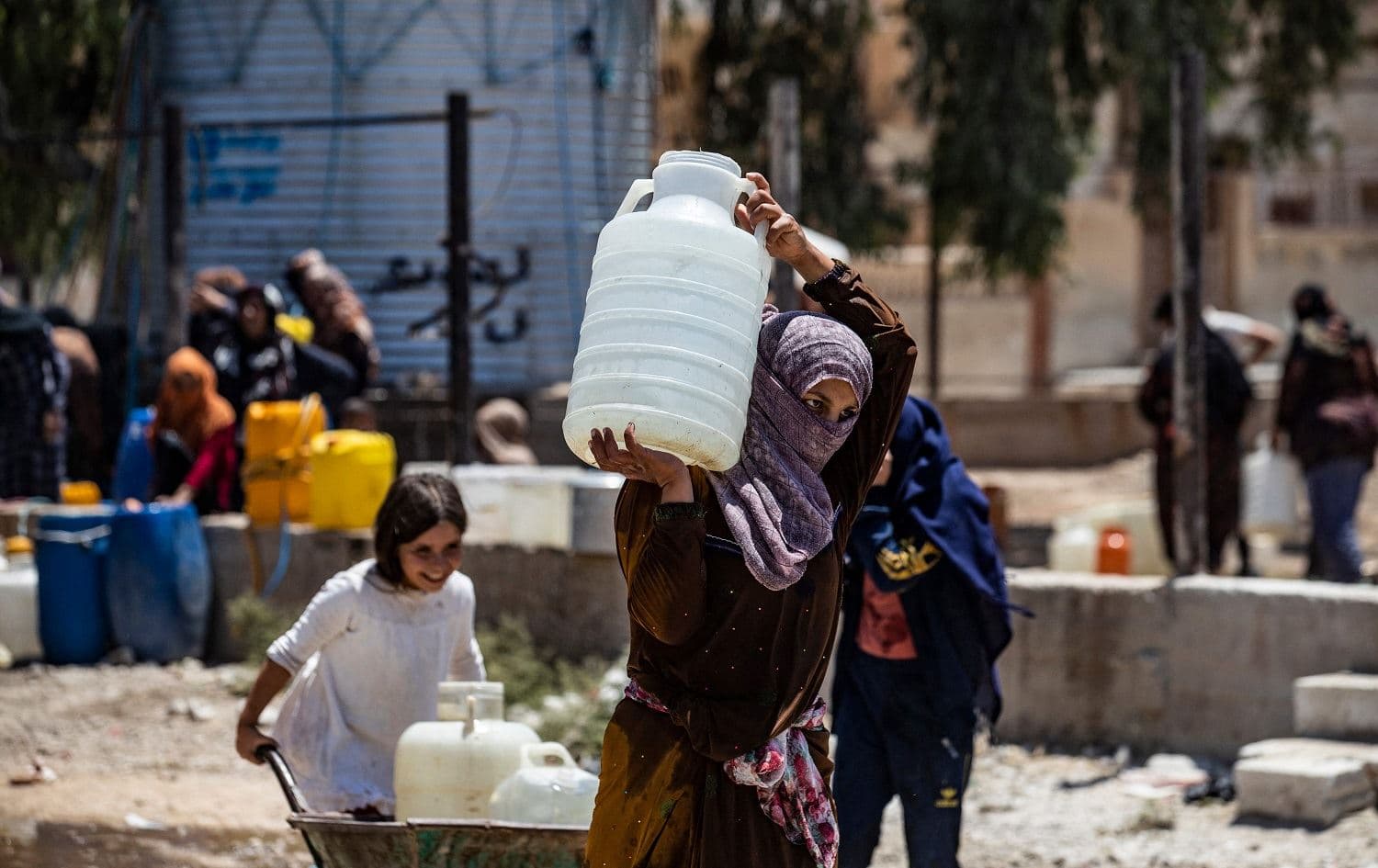 A Syrian woman carries a container of water provided by UNICEF in Hasaka on July 8, 2021, after disruption in the water supply from Alouk station. Photo: Delil Souleiman/AFP