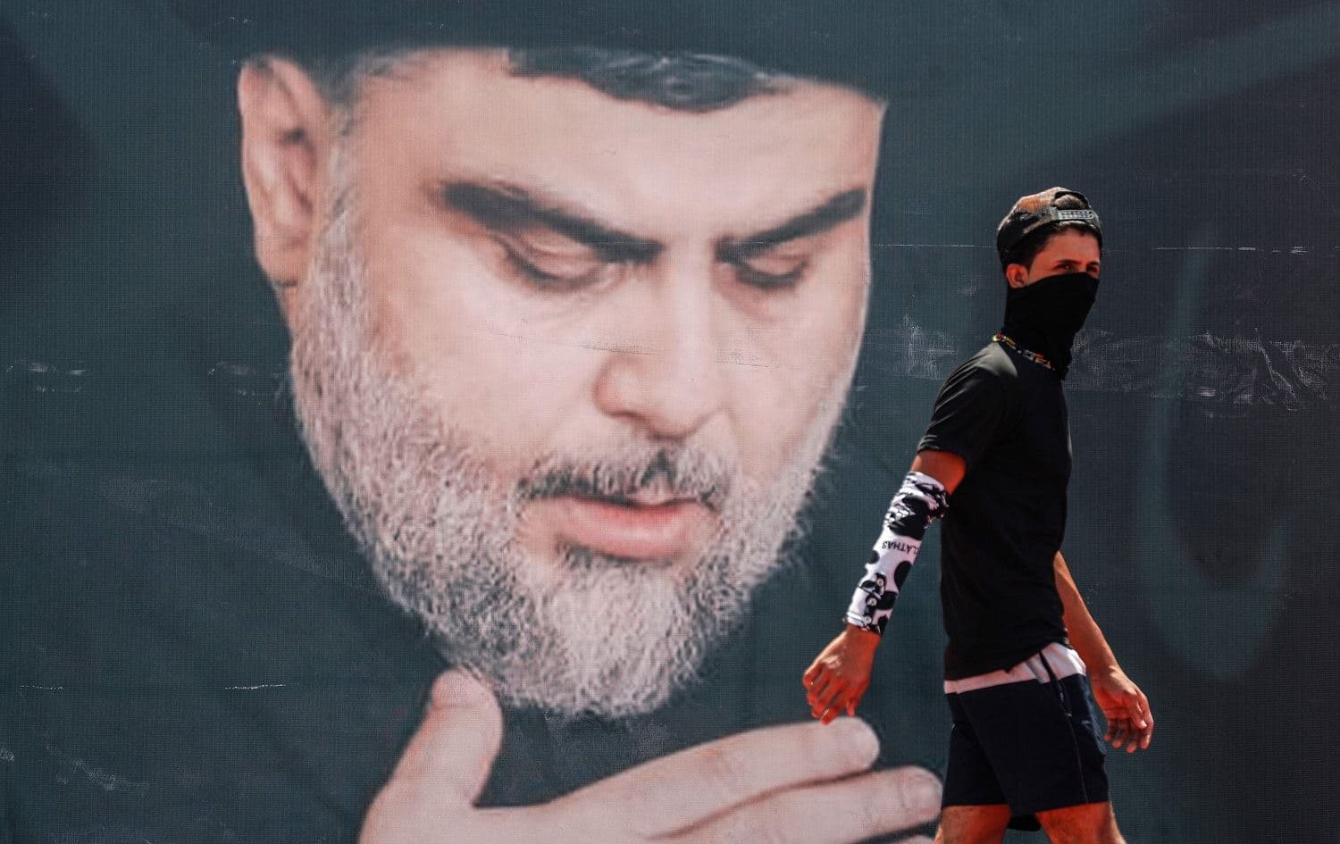 A mask-clad youth walks in front of a large poster of Iraq's populist Shiite Muslim cleric Muqtada al-Sadr in Sadr City, Baghdad, on July 15, 2021. File photo: Ahmad al-Rubaye/AFP