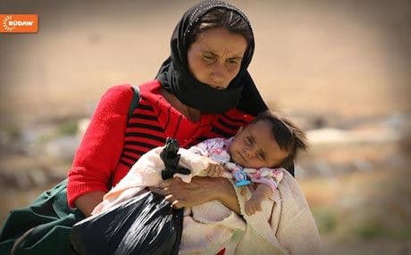A Yezidi woman carrying her baby reaches the Kurdistan Region after being rescued on Mount Shingal.
