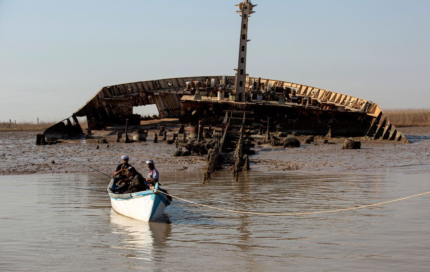 Iraqi men fish in their boat anchored in the Shatt al-Arab waterway next to the wreckage of a ship which was sunk during the 1980s Iraq-Iran war, near the southern Iraqi port city of al-Faw, on October 26, 2021. Hussein Faleh / AFP