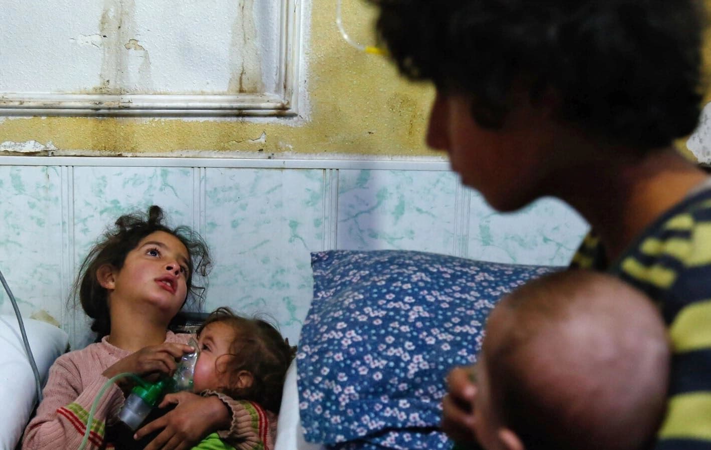 A Syrian girl holds an oxygen mask over the face of an infant at a make-shift hospital following a reported gas attack on the rebel-held besieged town of Douma in the eastern Ghouta region on the outskirts of the capital Damascus on January 22, 2018. Photo: AFP