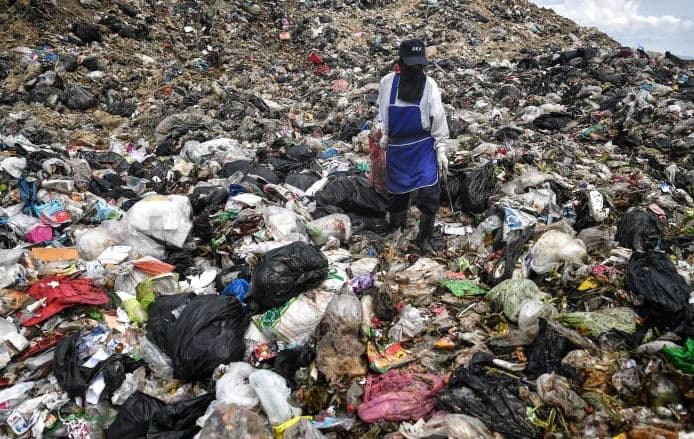 A garbage worker stands in a mound of trash in 2020. Photo: Lillian Suwanrumpha/AFP