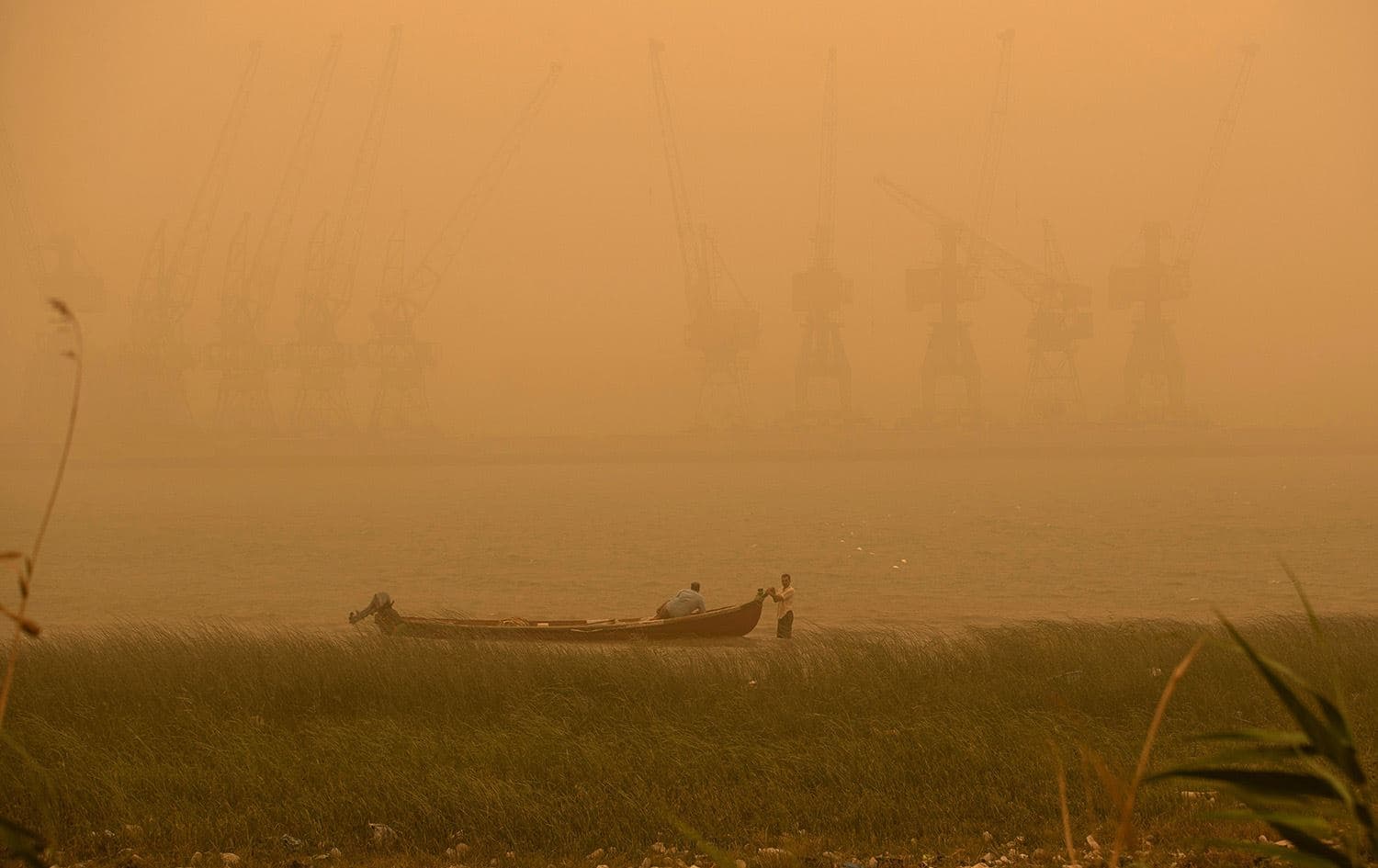 Fishermen sit in a boat opposite the port of Basra during a sandstorm sweeping through the country on May 23, 2022. Photo: Hussein Faleh/AFP