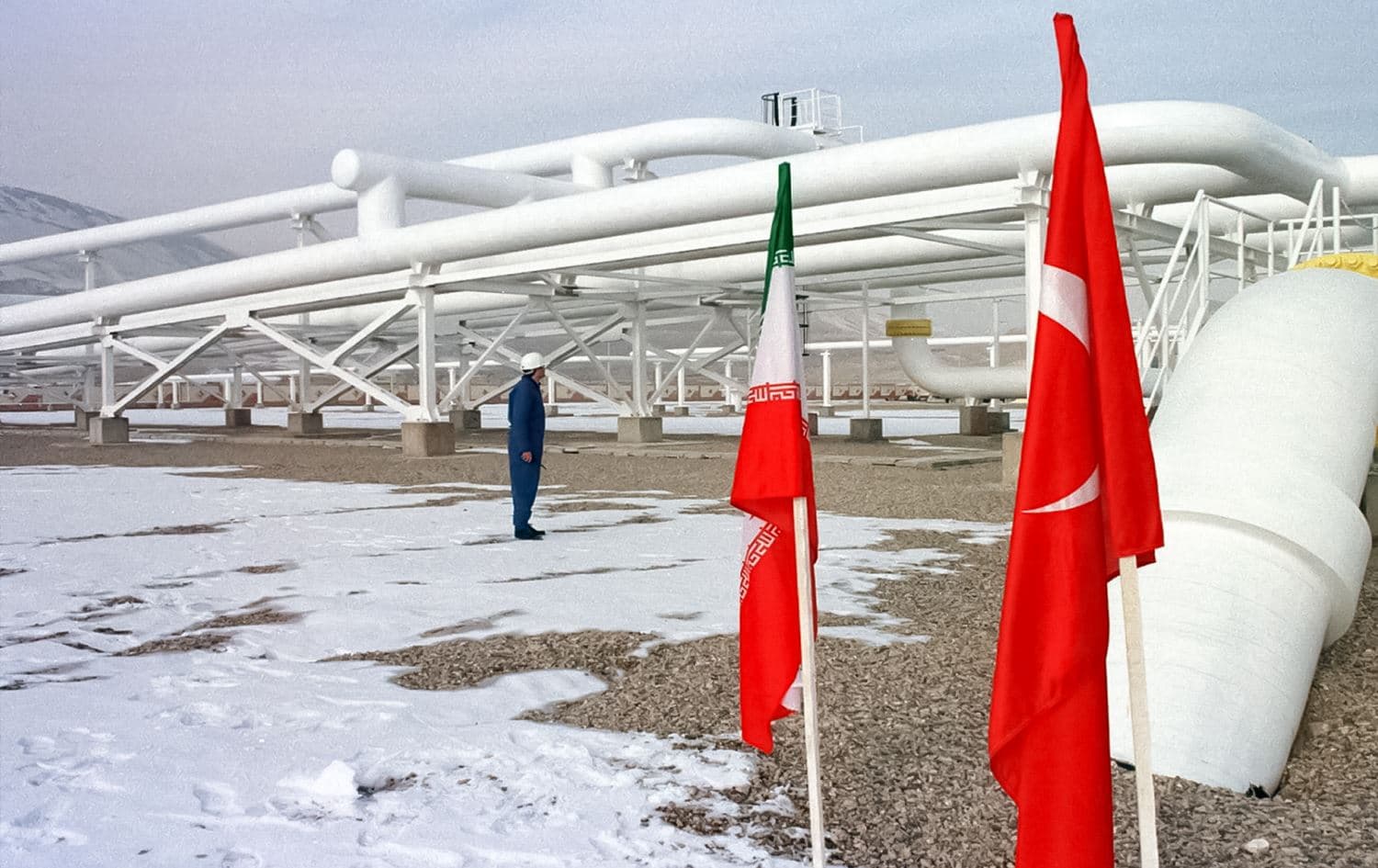 Iranian worker stands in front of gas pipelines next to flags of Turkey and Iran. Photo: AFP