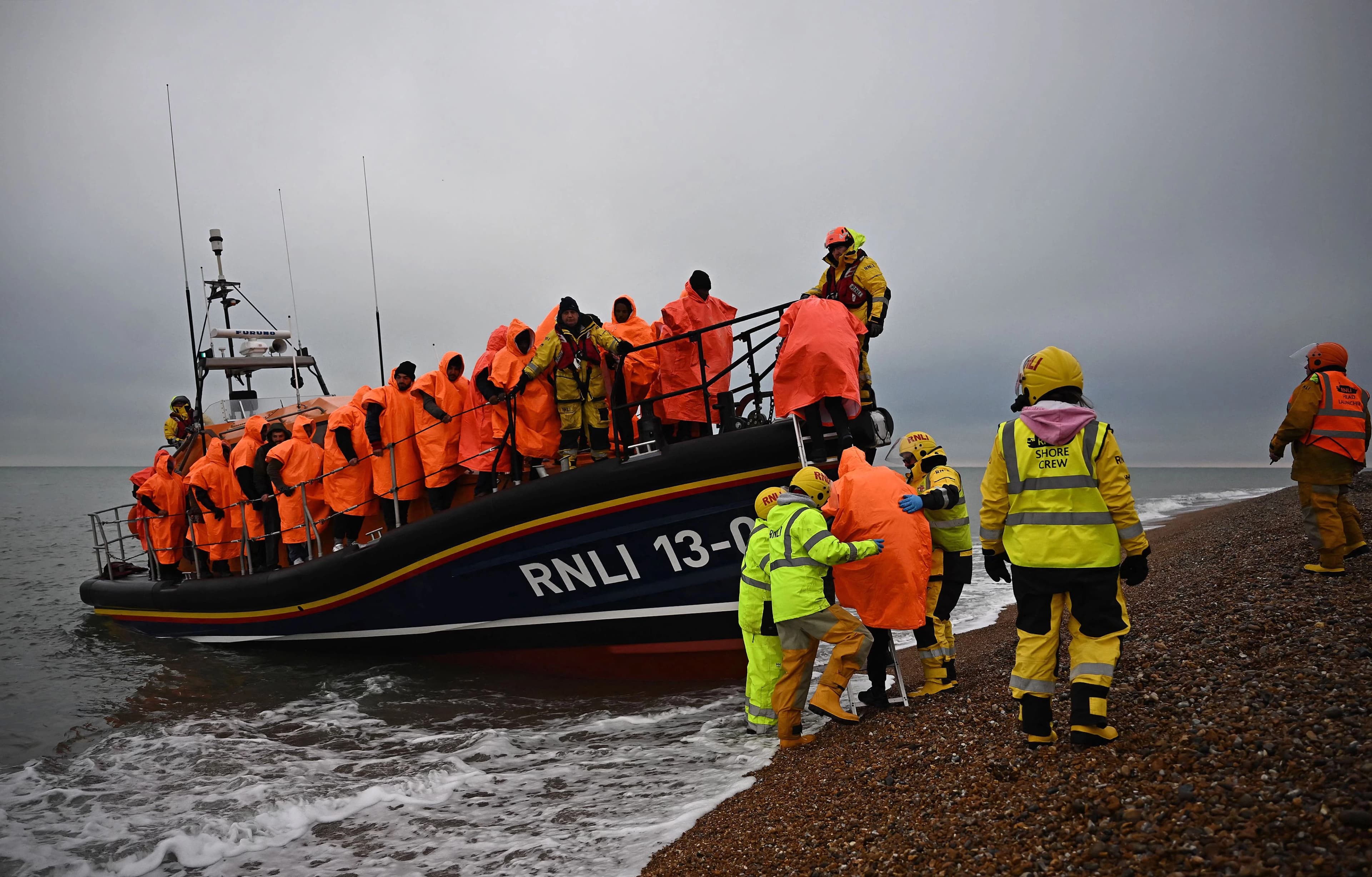 Migrants, picked up at sea attempting to cross the English Channel, are helped ashore from a RNLI lifeboat, at Dungeness on the southeast coast of England, on June December 9, 2022. Photo: AFP