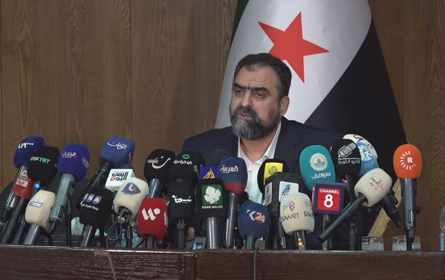 حەسەن سۆفان، ئەندامی لیژنەی باڵای ئاشتەوایی نیشتمانیی سووریا لە کۆنفرانسێکی رۆژنامەڤانیدا لە دیمەشق قسە دەکات