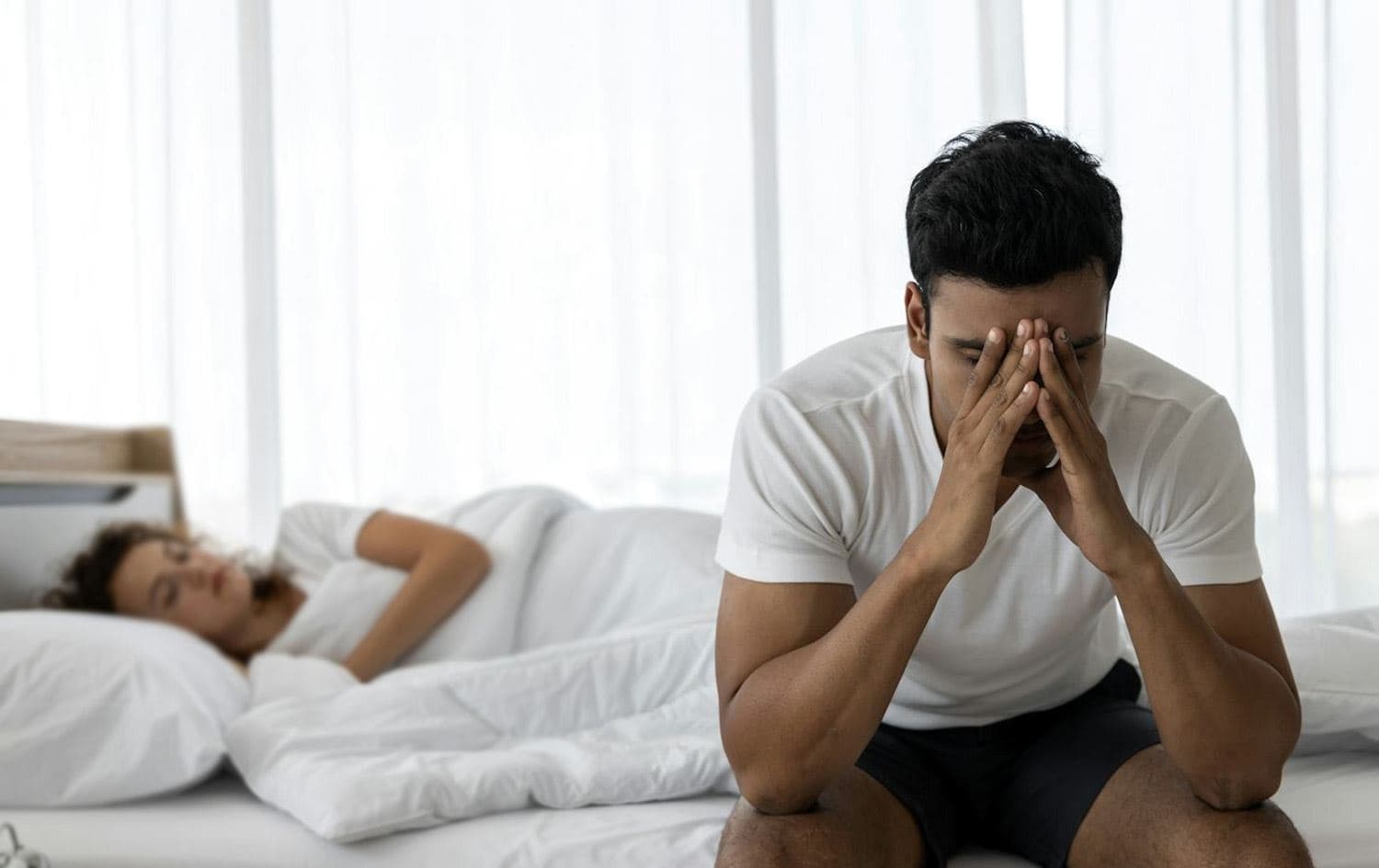 پیاوێک لەسەر جێگەی نووستنەکەی دانیشتووە و دڵەڕاوکێی پێوە دیارە.