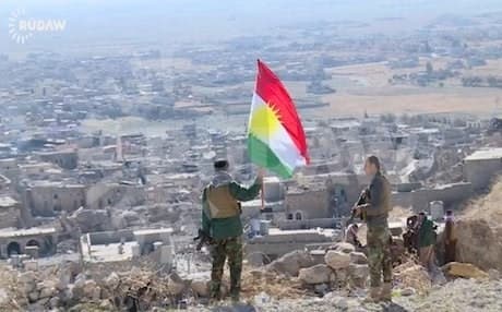 A Kurdish Peshmerga soldier holding a Kurdistan flag on Mount Shingal. Photo: Rudaw