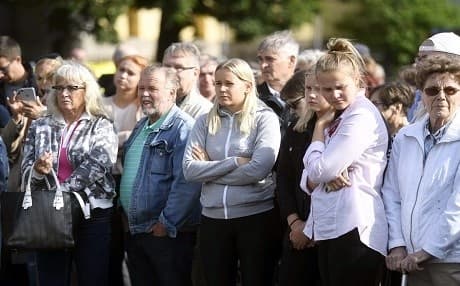 People hold a minute's silence in front of flowers and candles laid at a makeshift memorial at the Turku Market Square in Finland on Sunday. Photo: Vesa Moilanen | AFP
