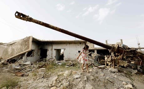 A Syrian child walks past a gun among destroyed buildings in Kobane on May 27, 2018. Photo: Delil Souleiman / AFP